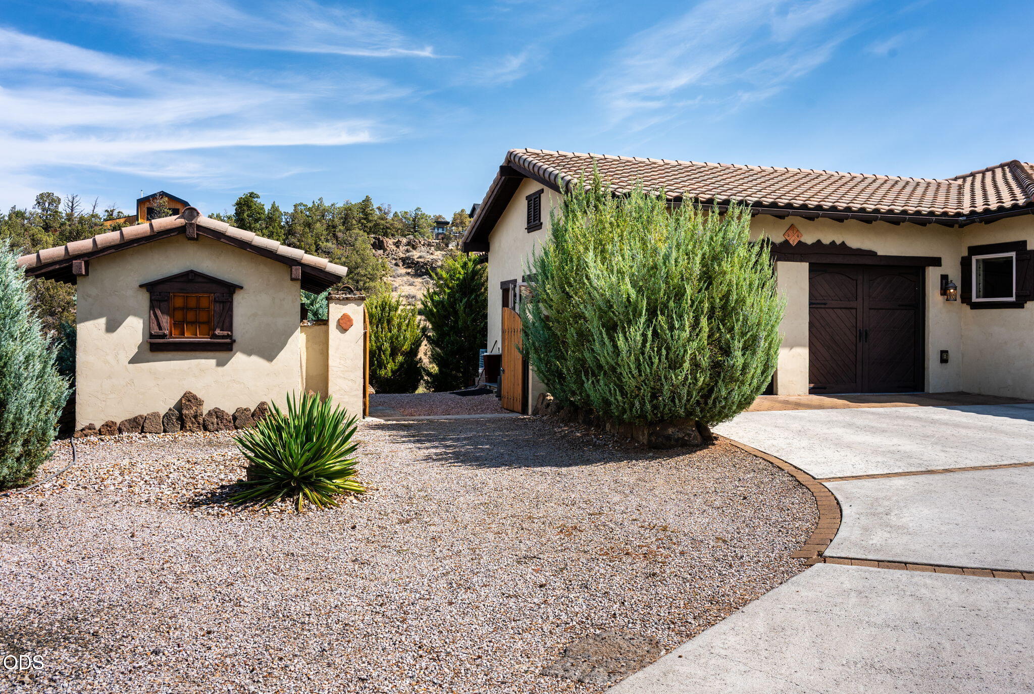 Stucco home with a tile roof, dark double garage doors, and a gravel courtyard with desert landscaping.