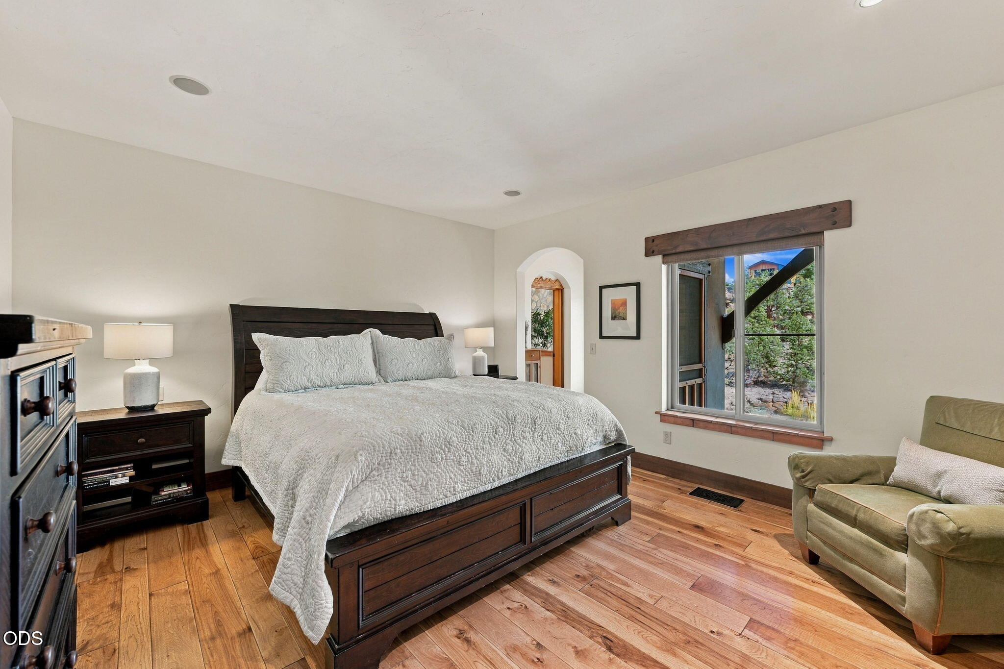 Bedroom with a dark wood bed, white quilt, hardwood floors, and a window overlooking trees.