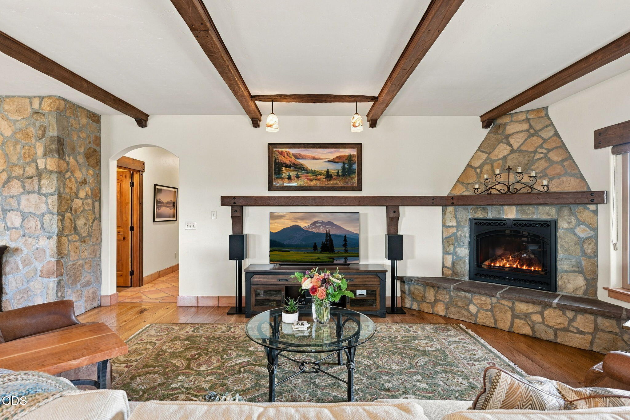 Living room with exposed wood beams, a stone fireplace, and a glass coffee table.