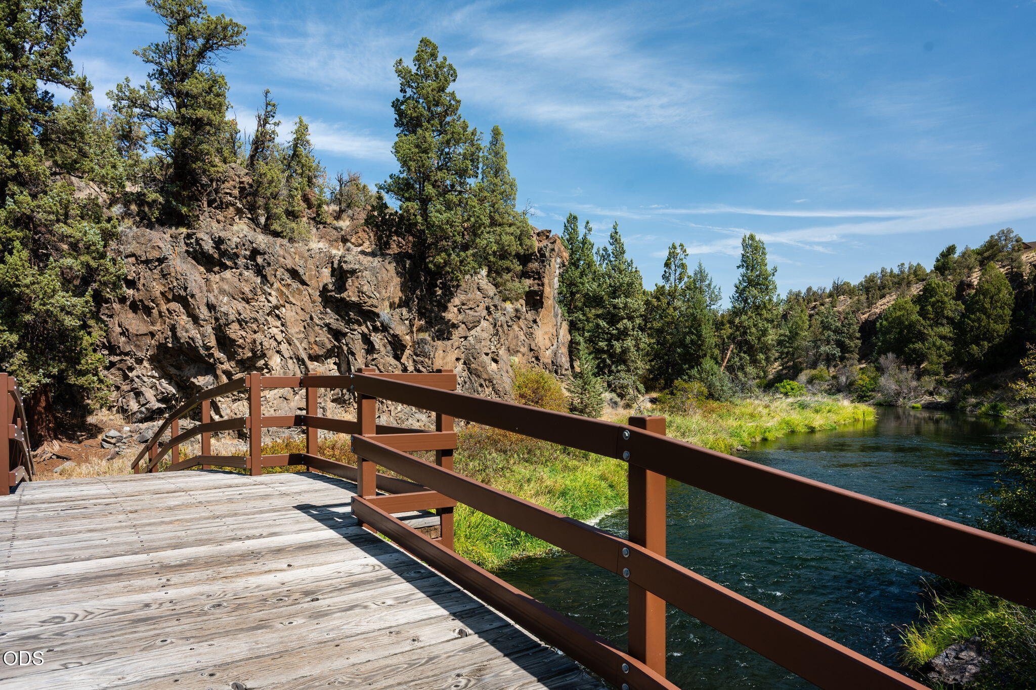 Riverside deck overlooking a flowing river beside a rocky, tree-covered cliff.