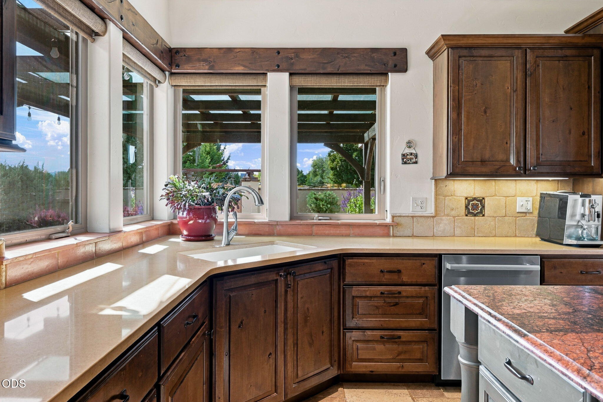 Kitchen with dark wood cabinets and a sink beneath large windows overlooking greenery and a covered patio.