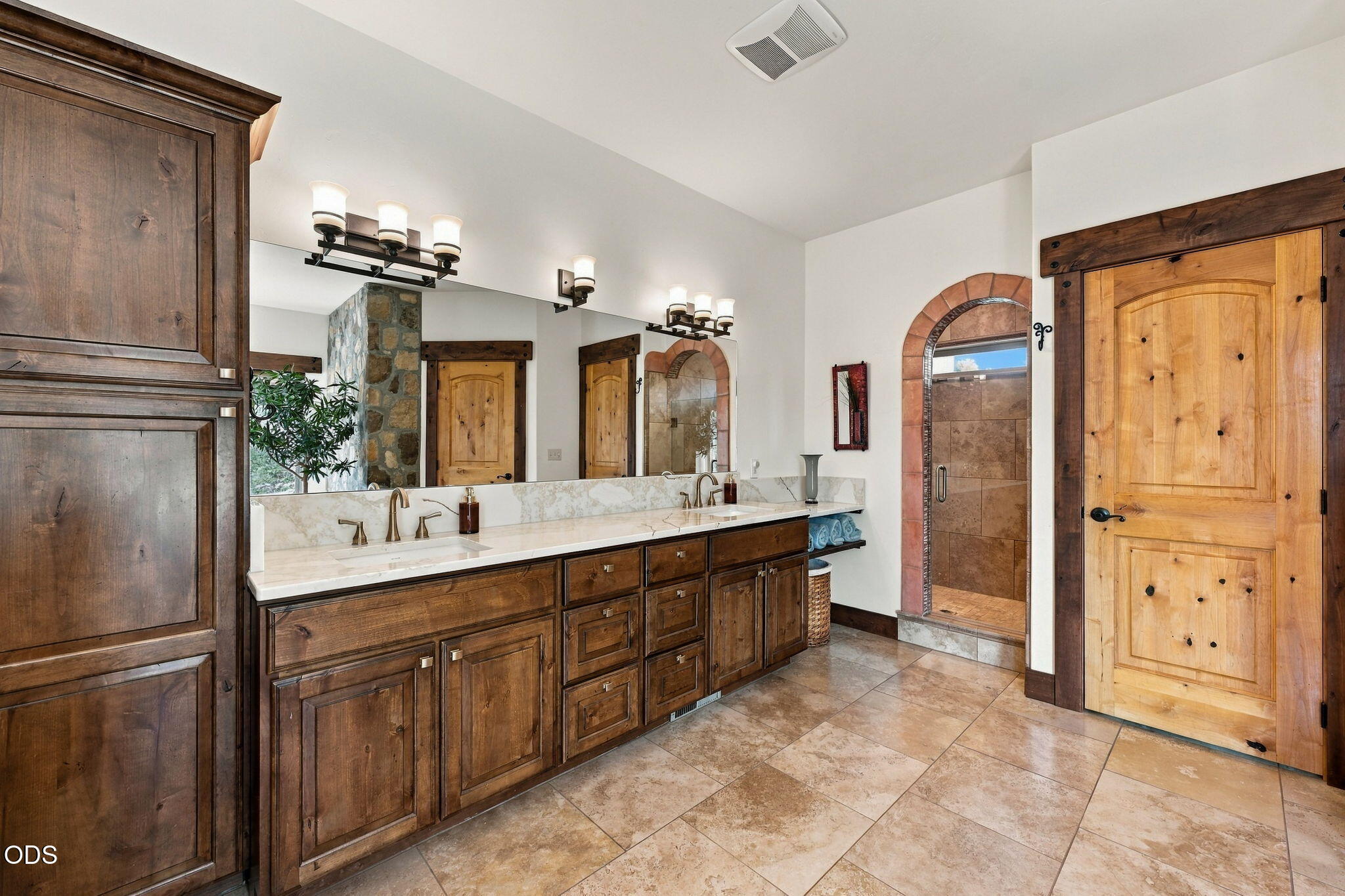 Bathroom with a double vanity, dark wood cabinets, and an arched tiled shower.