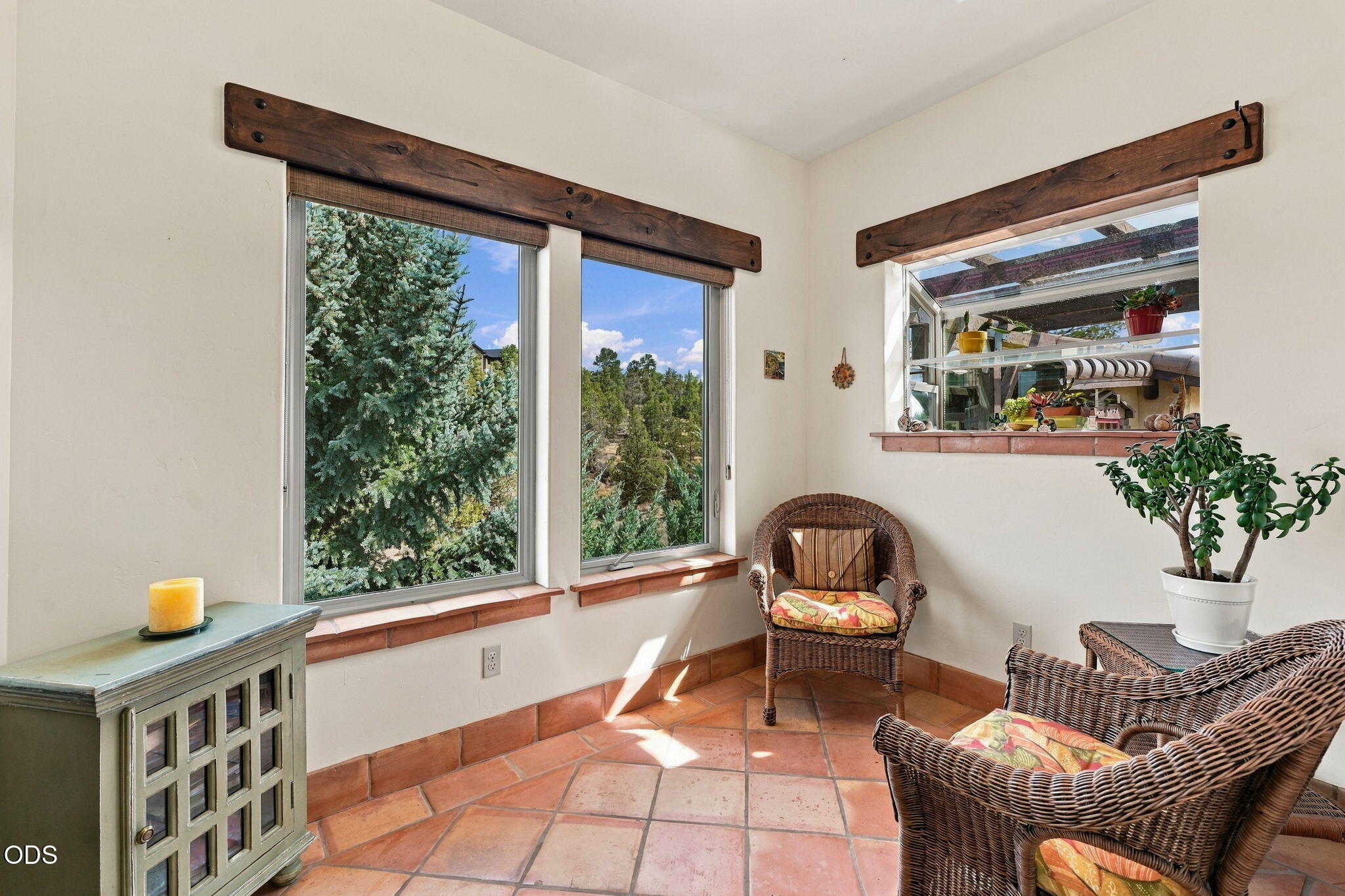 Furnished sunroom with wicker chairs, terracotta tile, and windows overlooking trees.