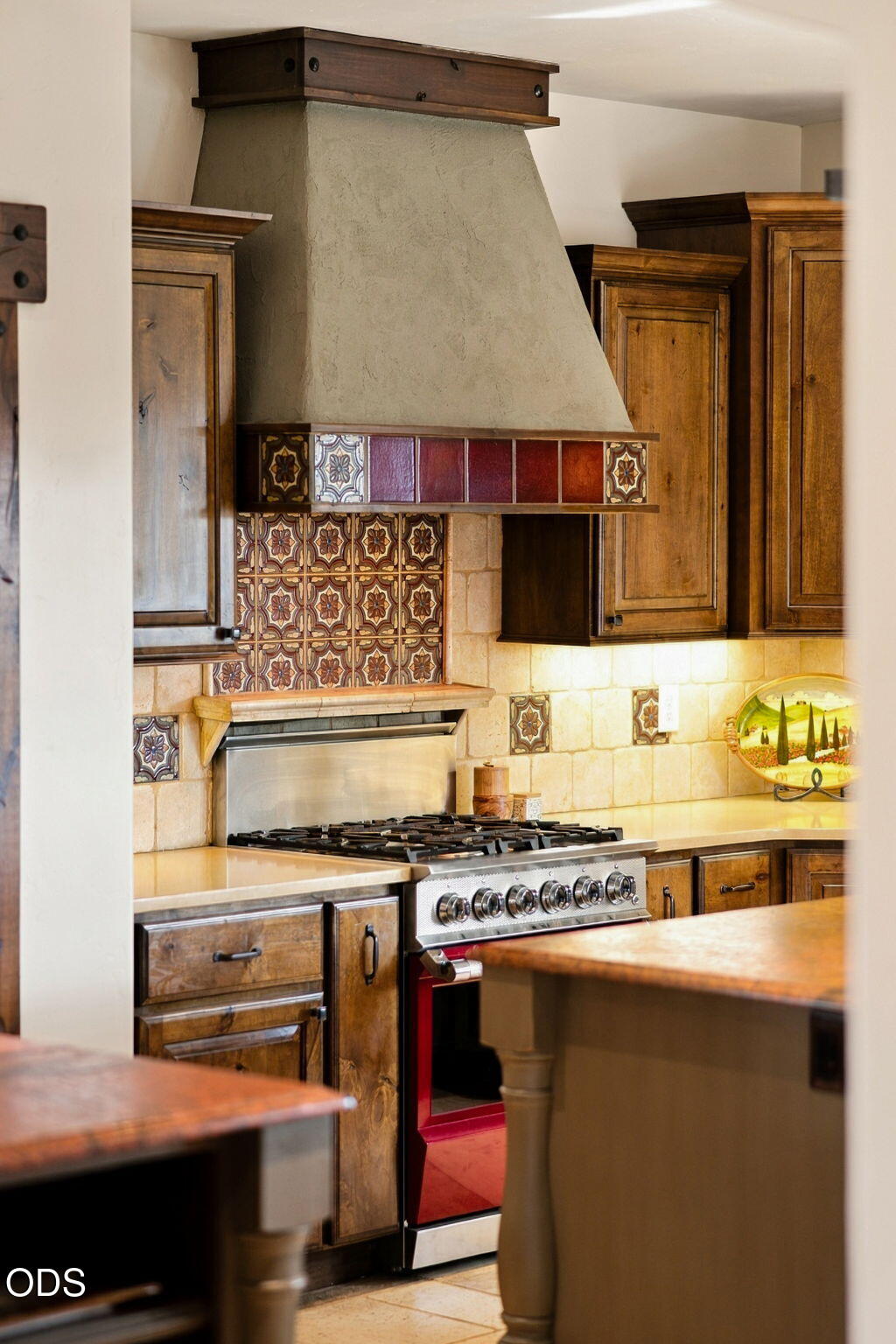 Kitchen with a plaster range hood, patterned tile backsplash, wood cabinets, and stainless-steel gas range.