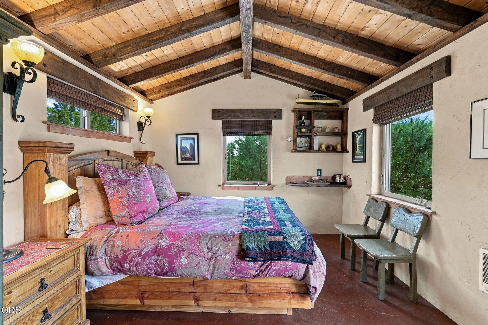 Furnished bedroom with a timber vaulted ceiling, rustic bed, and woodland views through the windows.