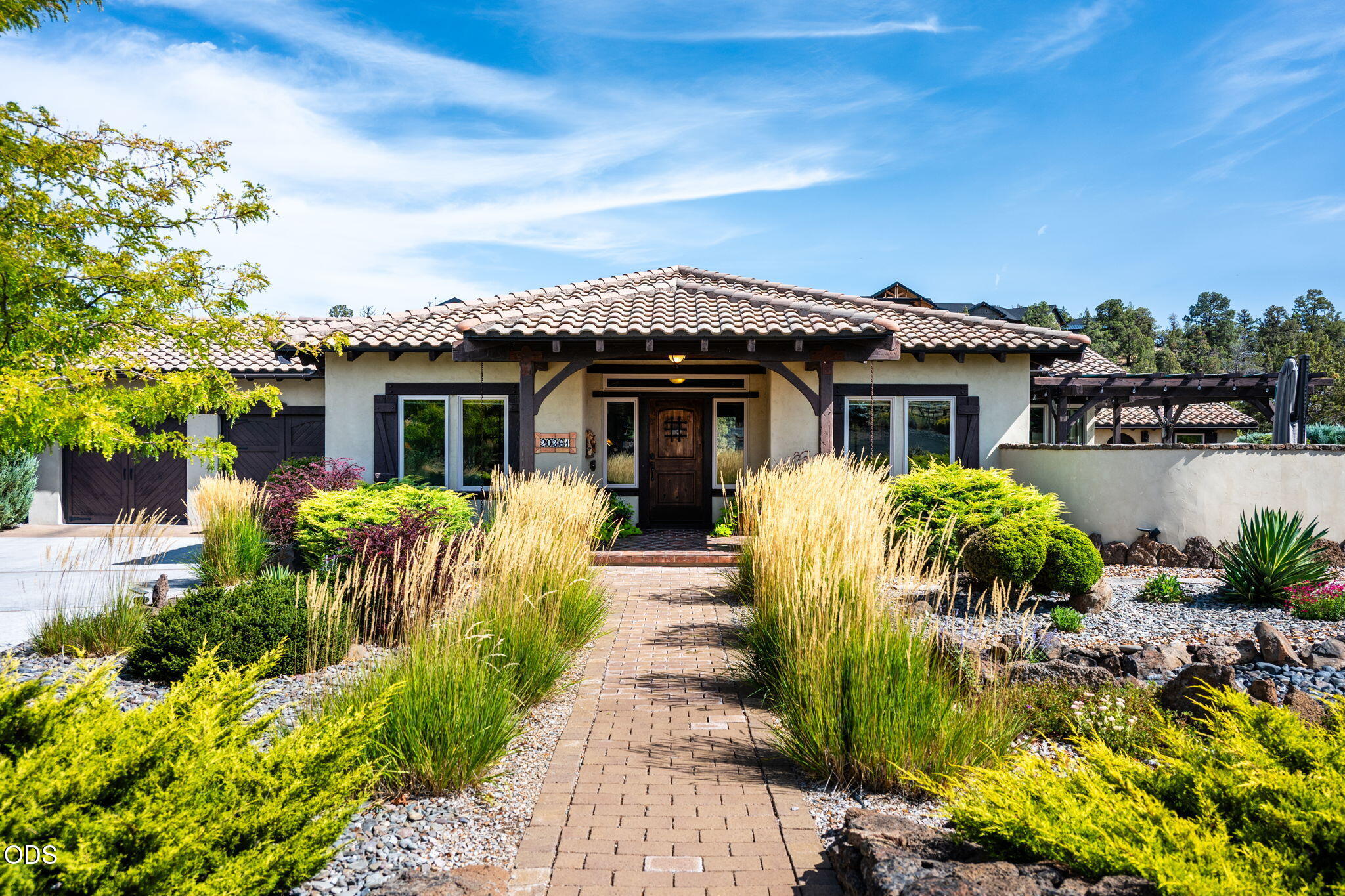 Home with a tiled roof and covered entry, approached by a brick walkway through landscaped ornamental grasses.