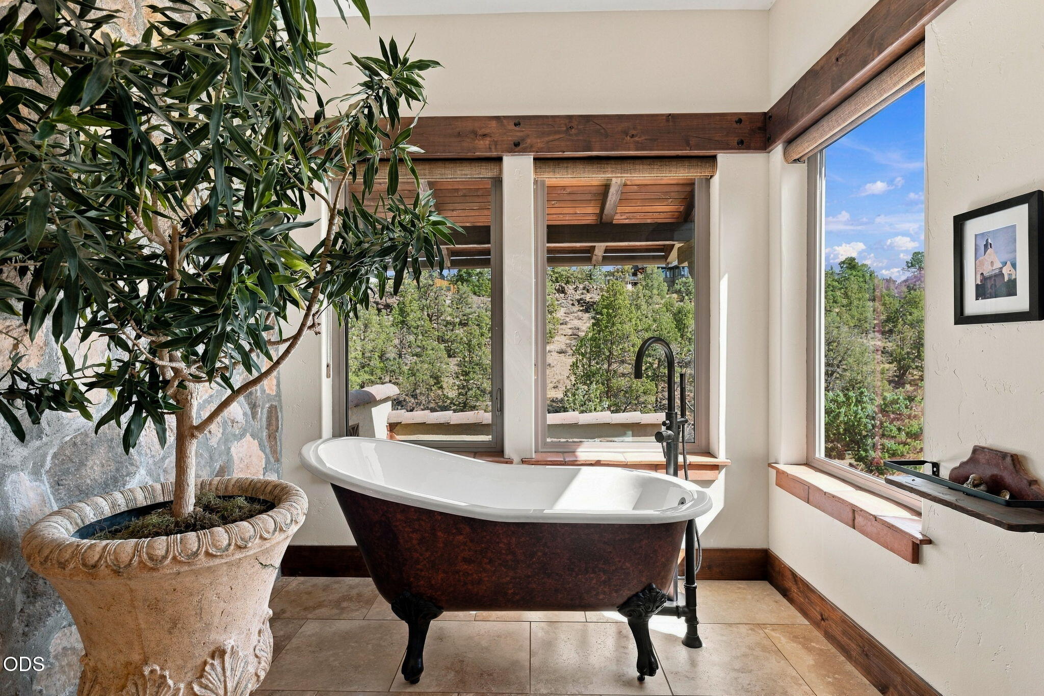 Bathroom with a freestanding clawfoot tub and wide windows overlooking a wooded hillside.
