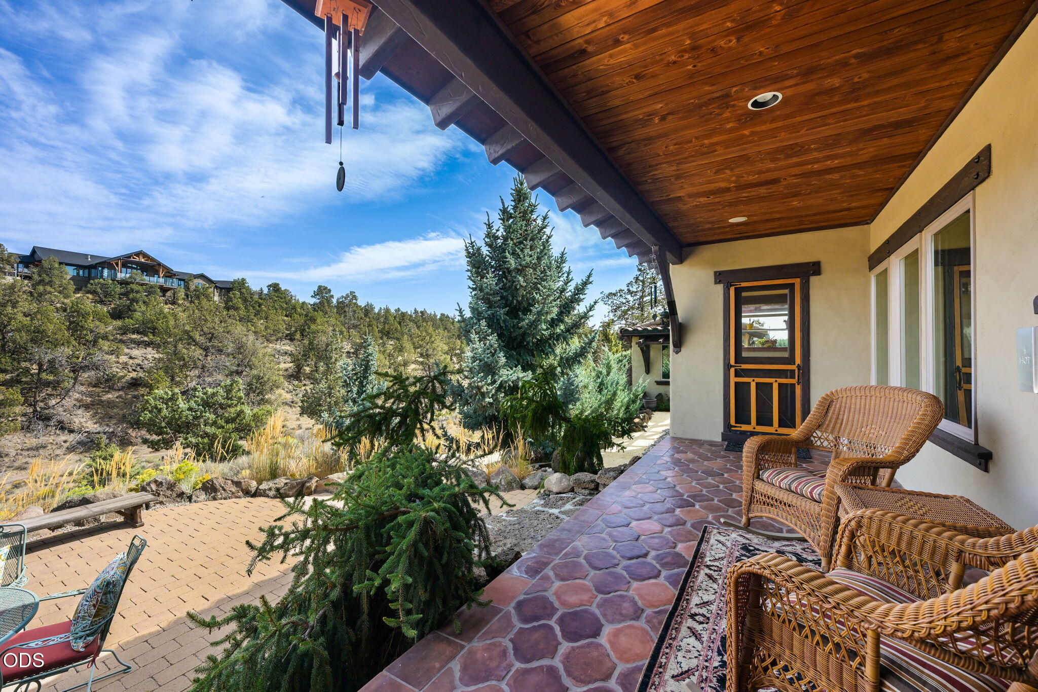 Covered patio with wicker chairs overlooking evergreen trees and a wooded hillside.