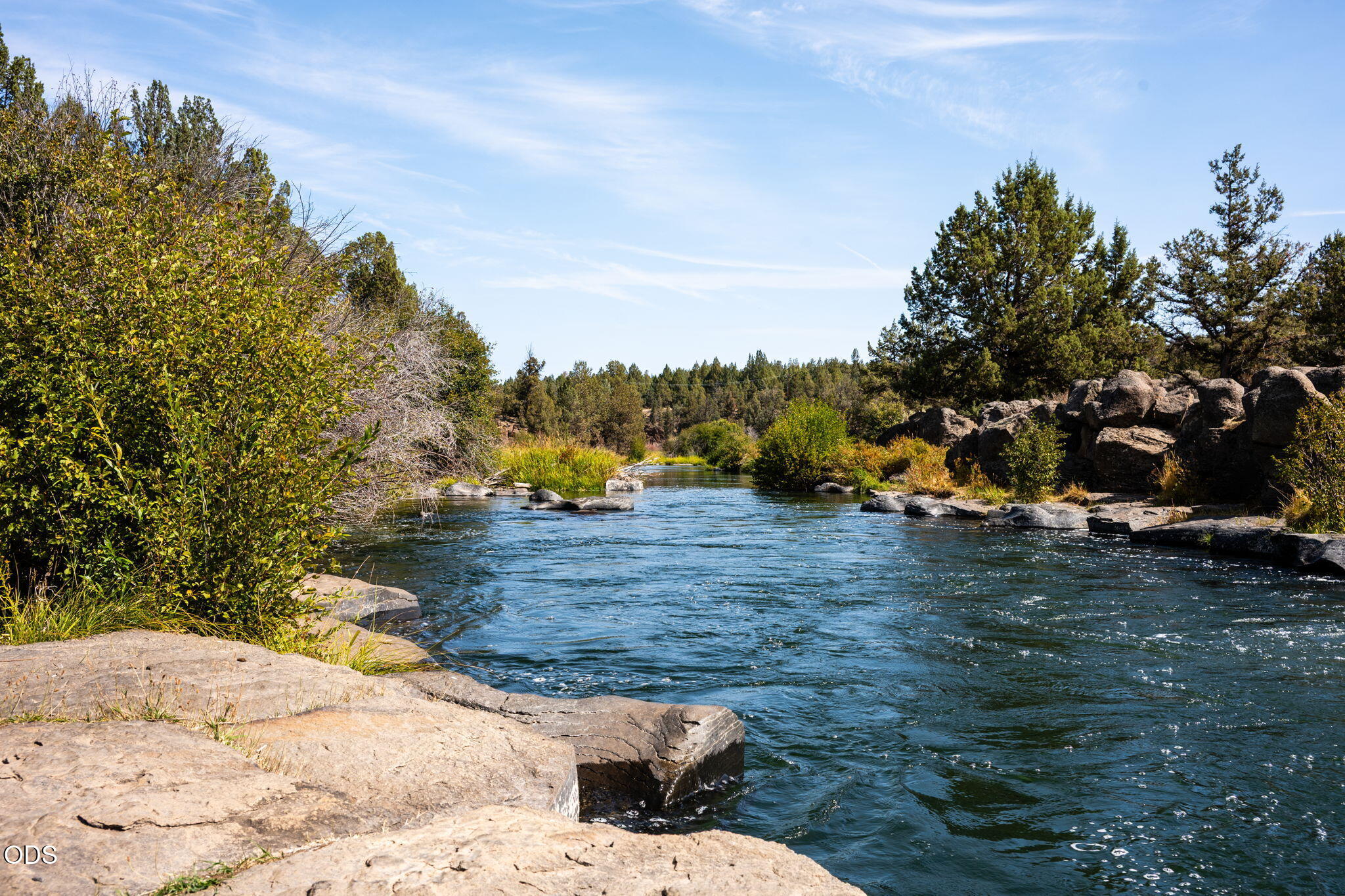 River flowing past broad rock shelves and boulders beneath evergreen trees.