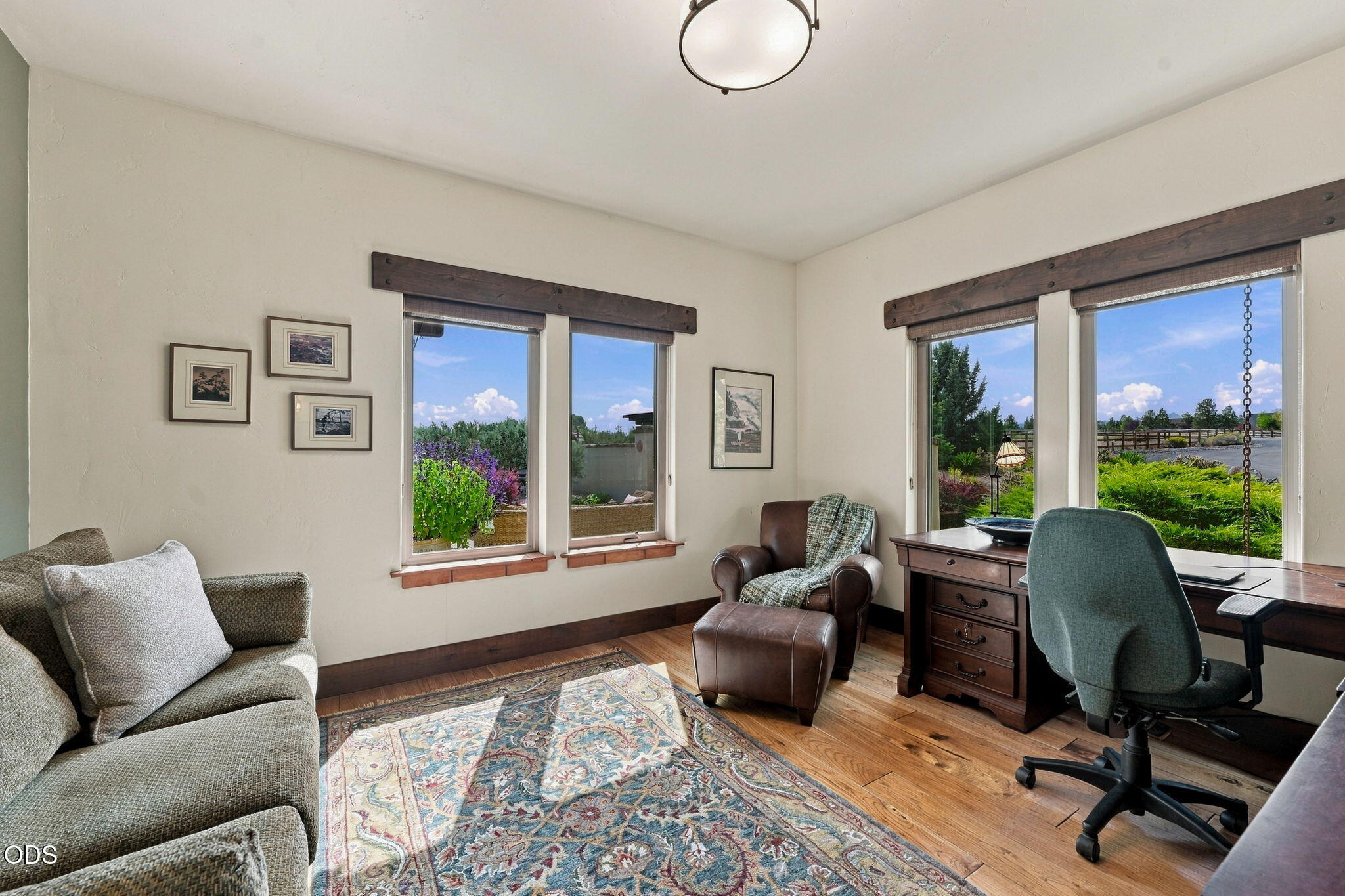 Home office with a wooden desk, leather armchair, and large windows overlooking water and greenery.