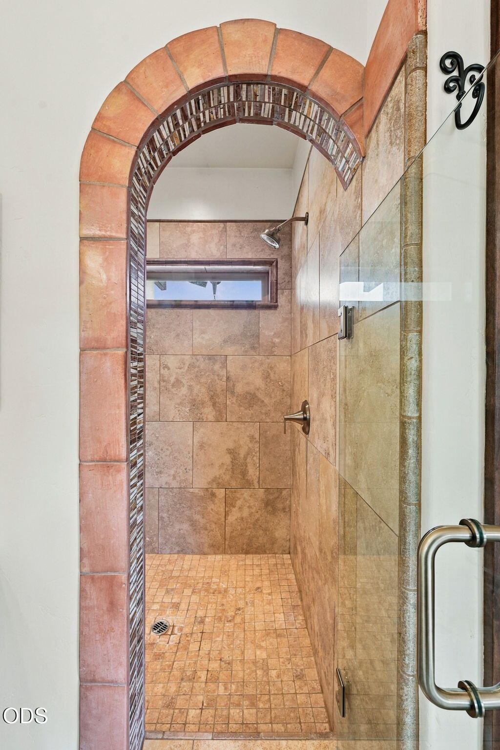 Walk-in shower with warm stone tile, glass enclosure, and a decorative arched entry.