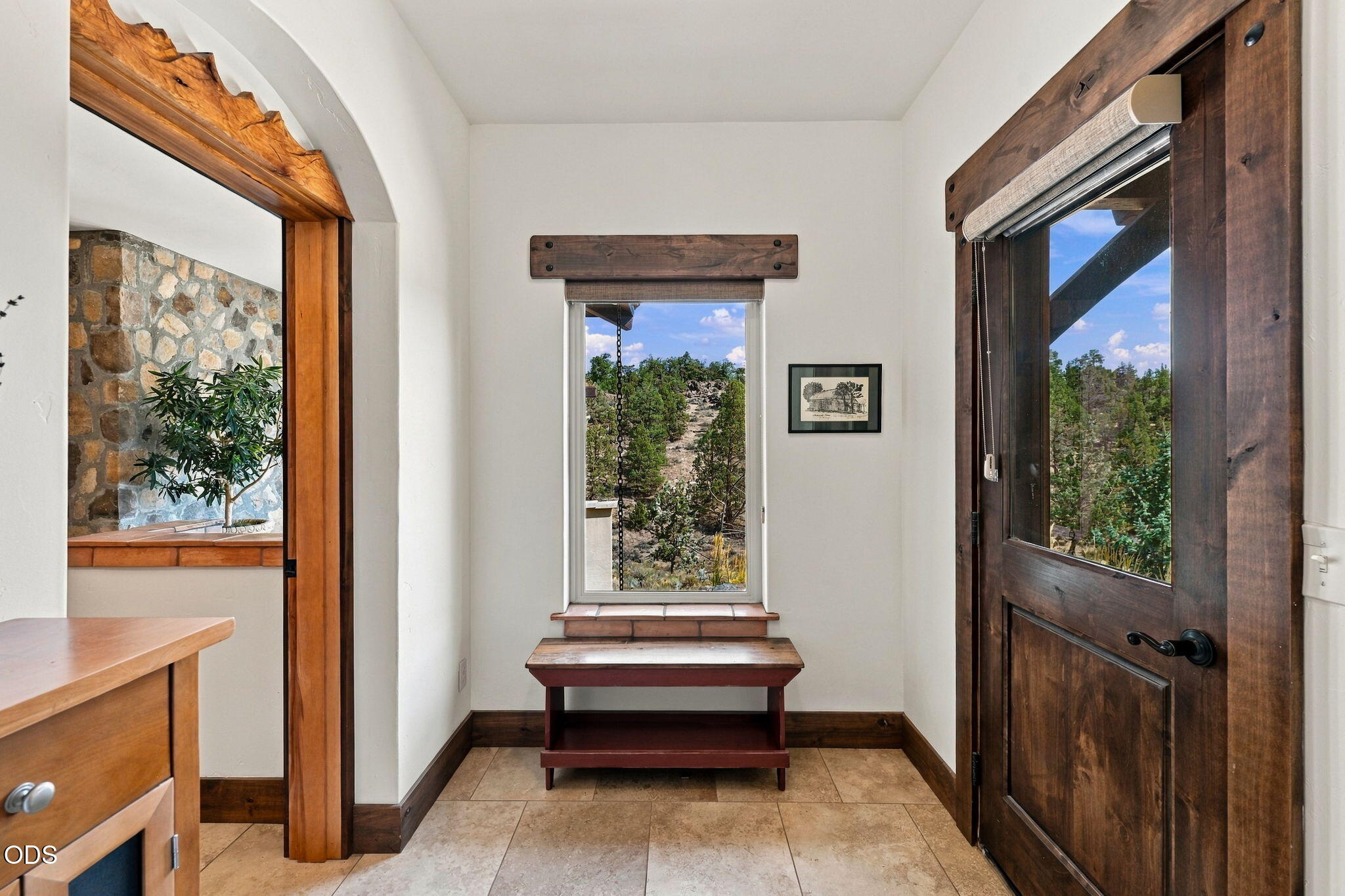 Entry foyer with a dark wood front door, window-side bench, and views of rocky, tree-covered land.