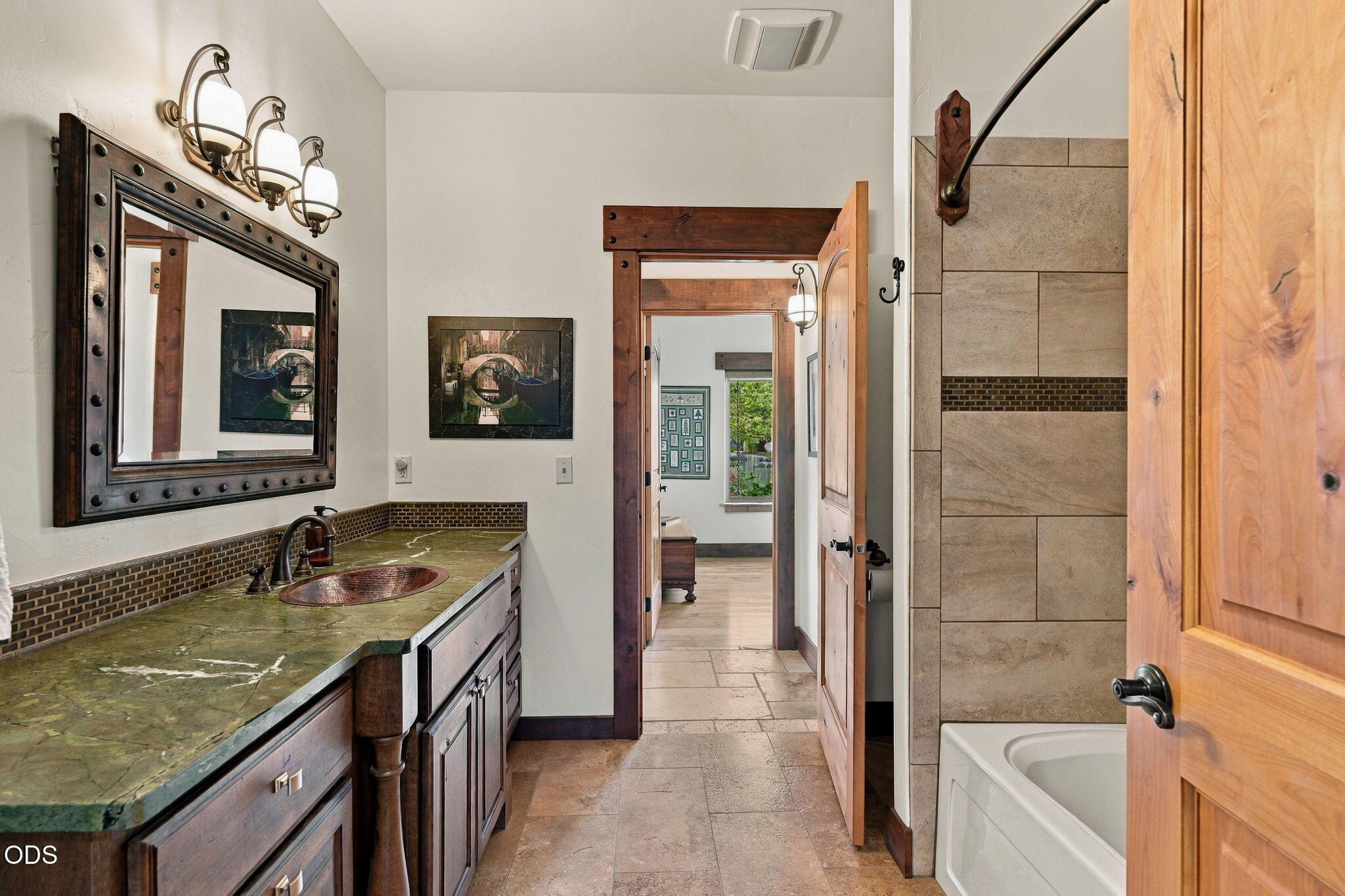 Bathroom with a green stone vanity and copper sink beside a tiled bathtub.