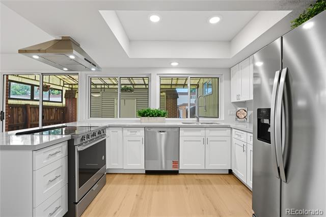 Bright white kitchen with stainless steel appliances, light wood floors, and windows overlooking a fenced patio.