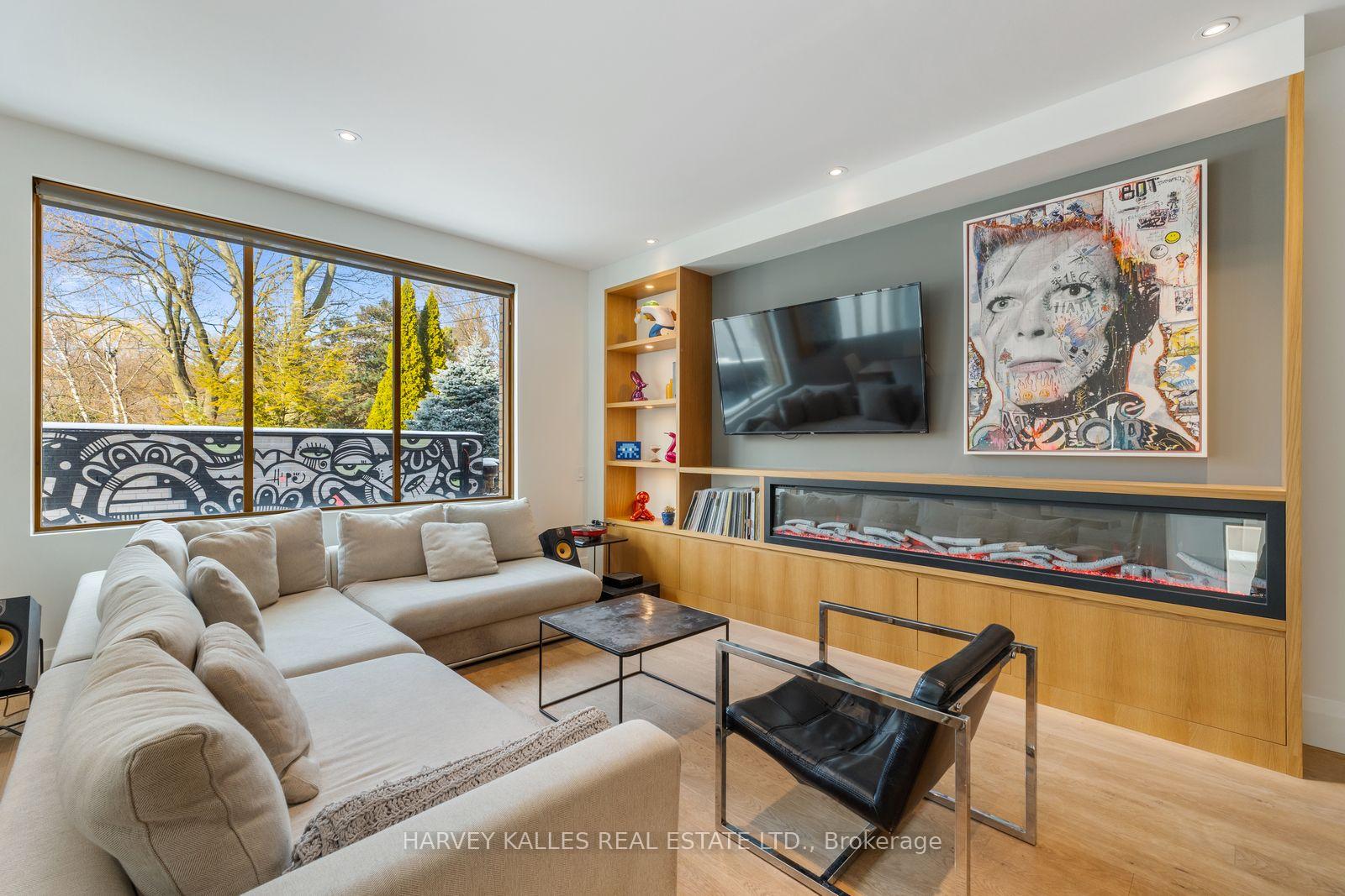 Living room with a large sectional, built-in linear fireplace, and wide windows overlooking trees.
