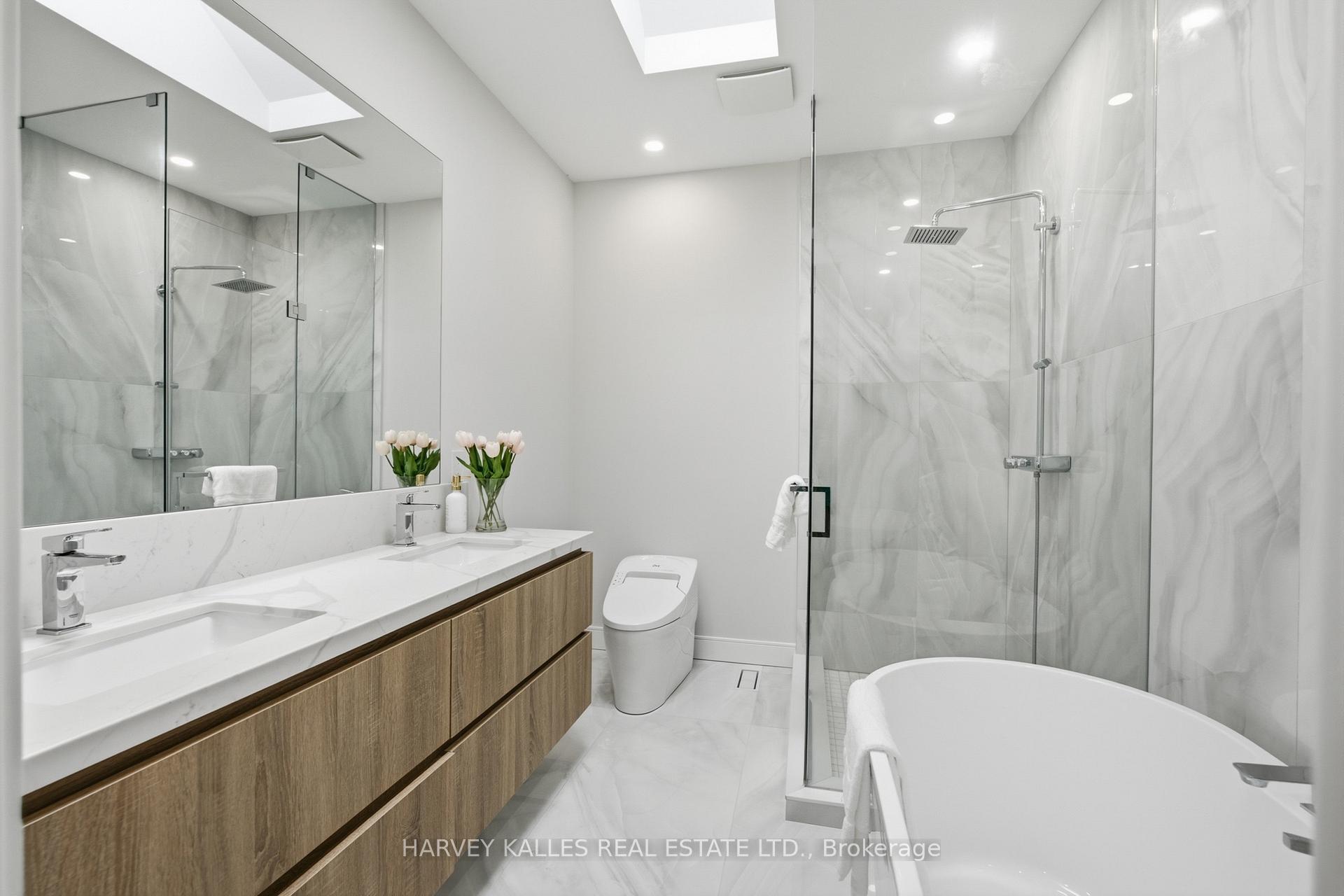 Modern bathroom with a double vanity, marble-look tile, glass shower, and freestanding soaking tub.