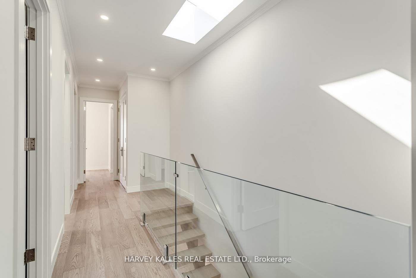 Bright hallway and stair landing with pale wood floors, glass railing, and skylights.