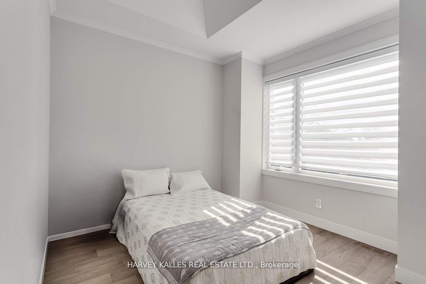 Bedroom with a white-and-gray bed, wood flooring, and a large sunlit window.