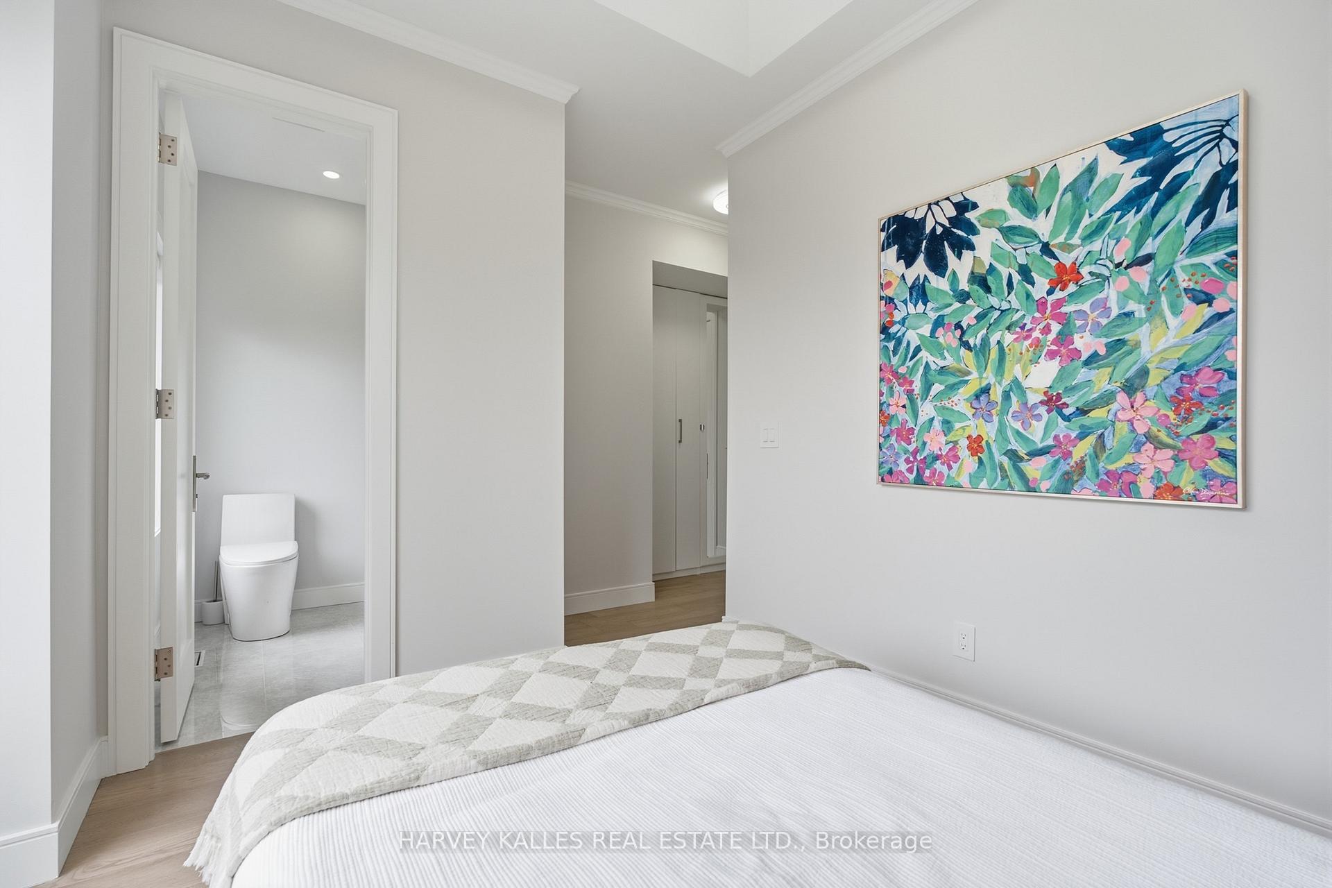 Bedroom with a white bed, colorful floral painting, and open doorway to an adjoining bathroom.
