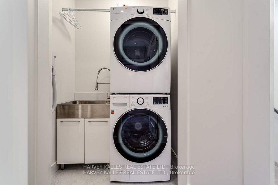Laundry room with stacked front-loading washer and dryer beside a stainless utility sink.