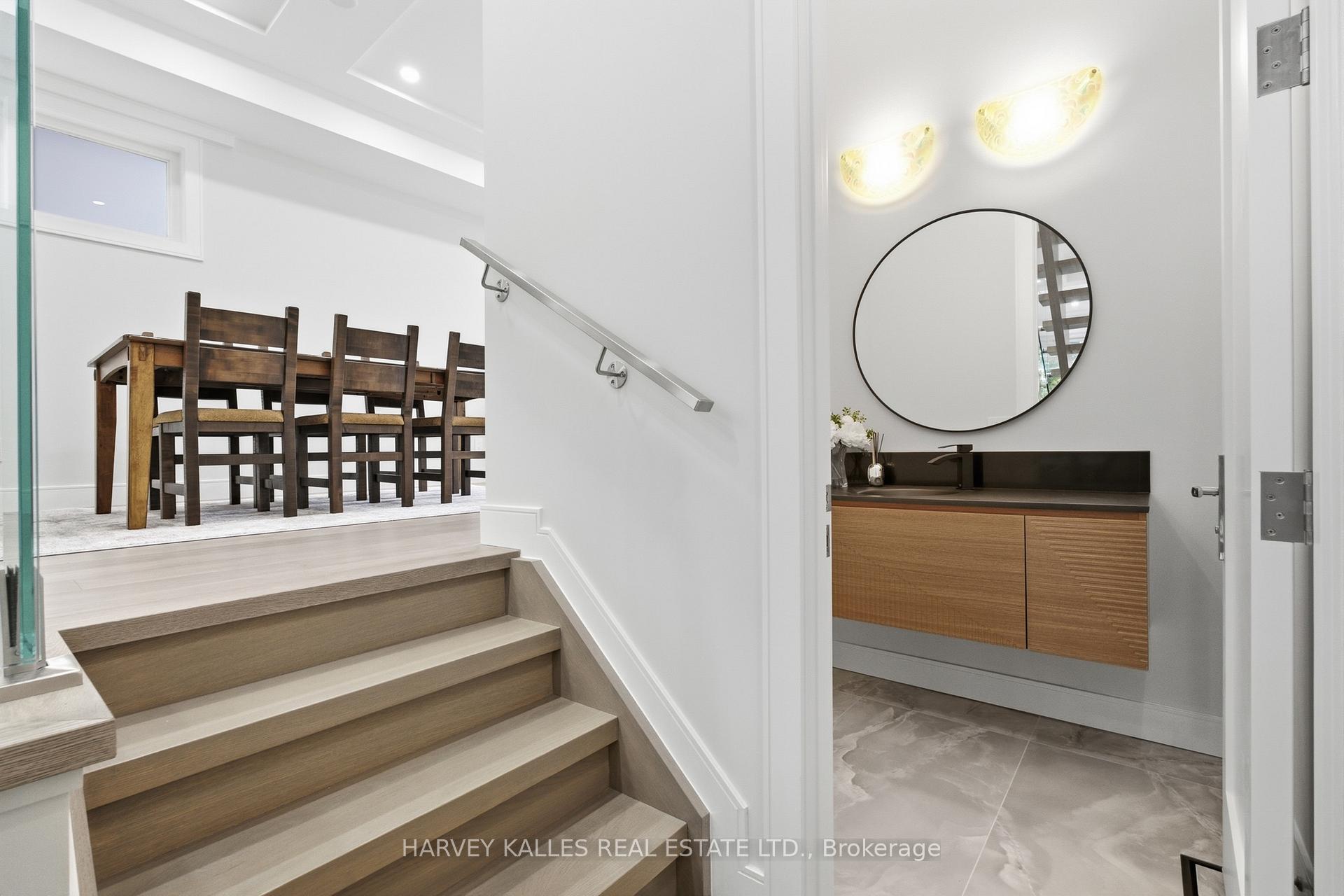Wood-toned stairs lead to a dining area beside a powder room with a round mirror.