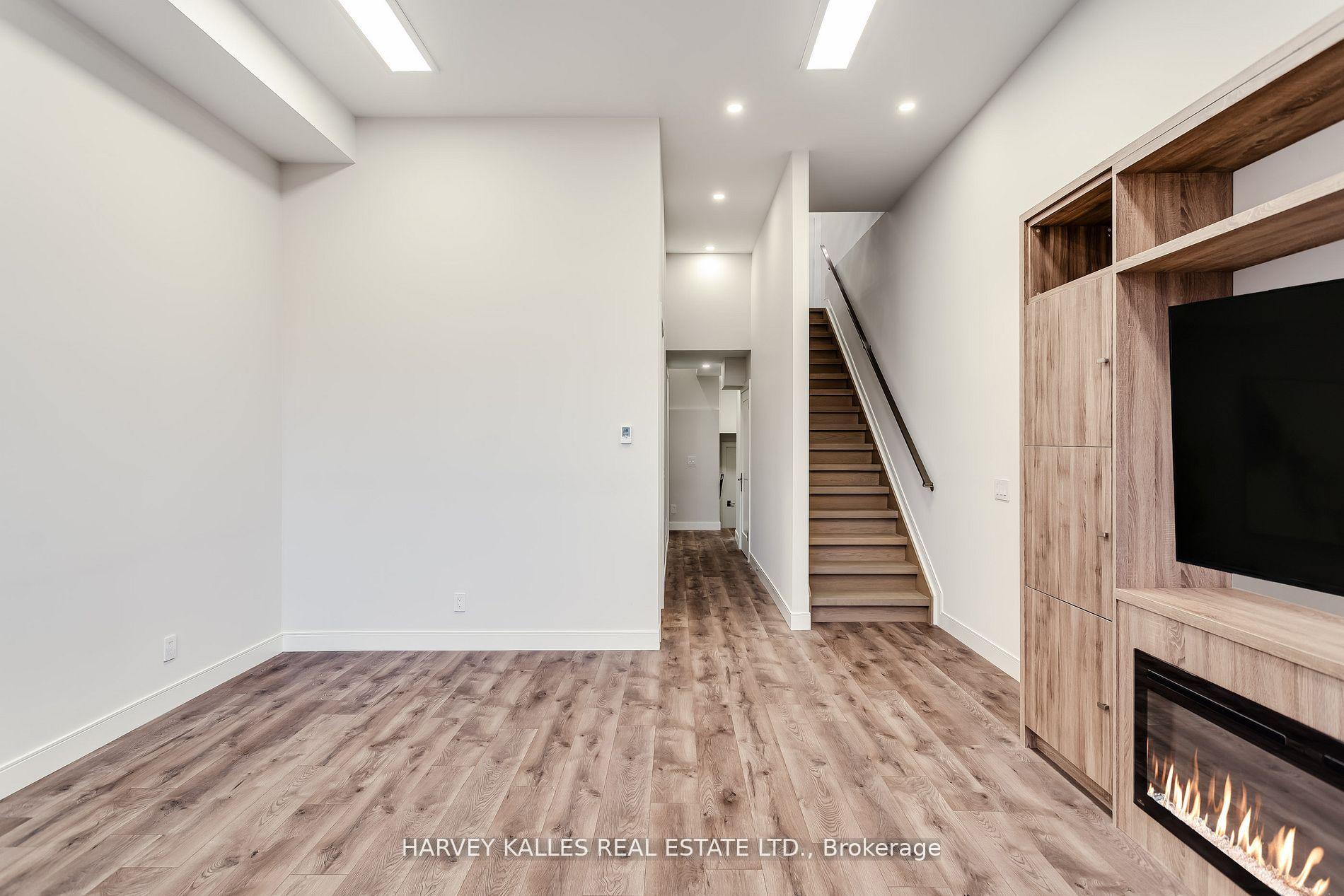 Unfurnished living room with wood flooring, staircase, and built-in entertainment unit with fireplace.
