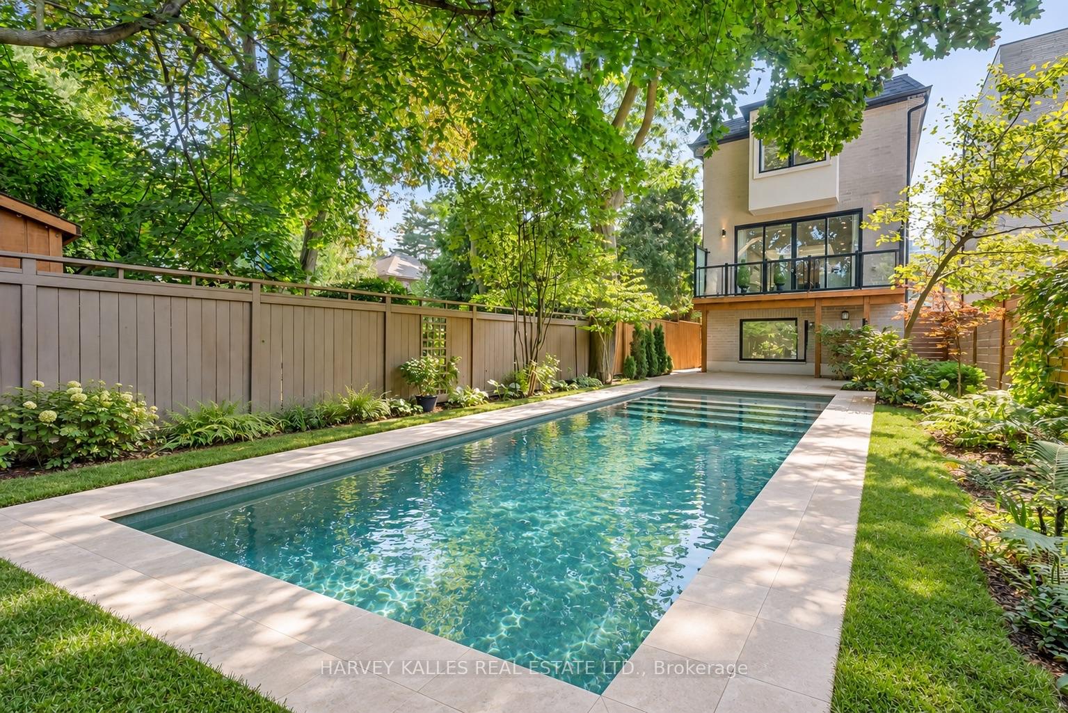 Backyard swimming pool beside a modern home, framed by mature trees and landscaped gardens.