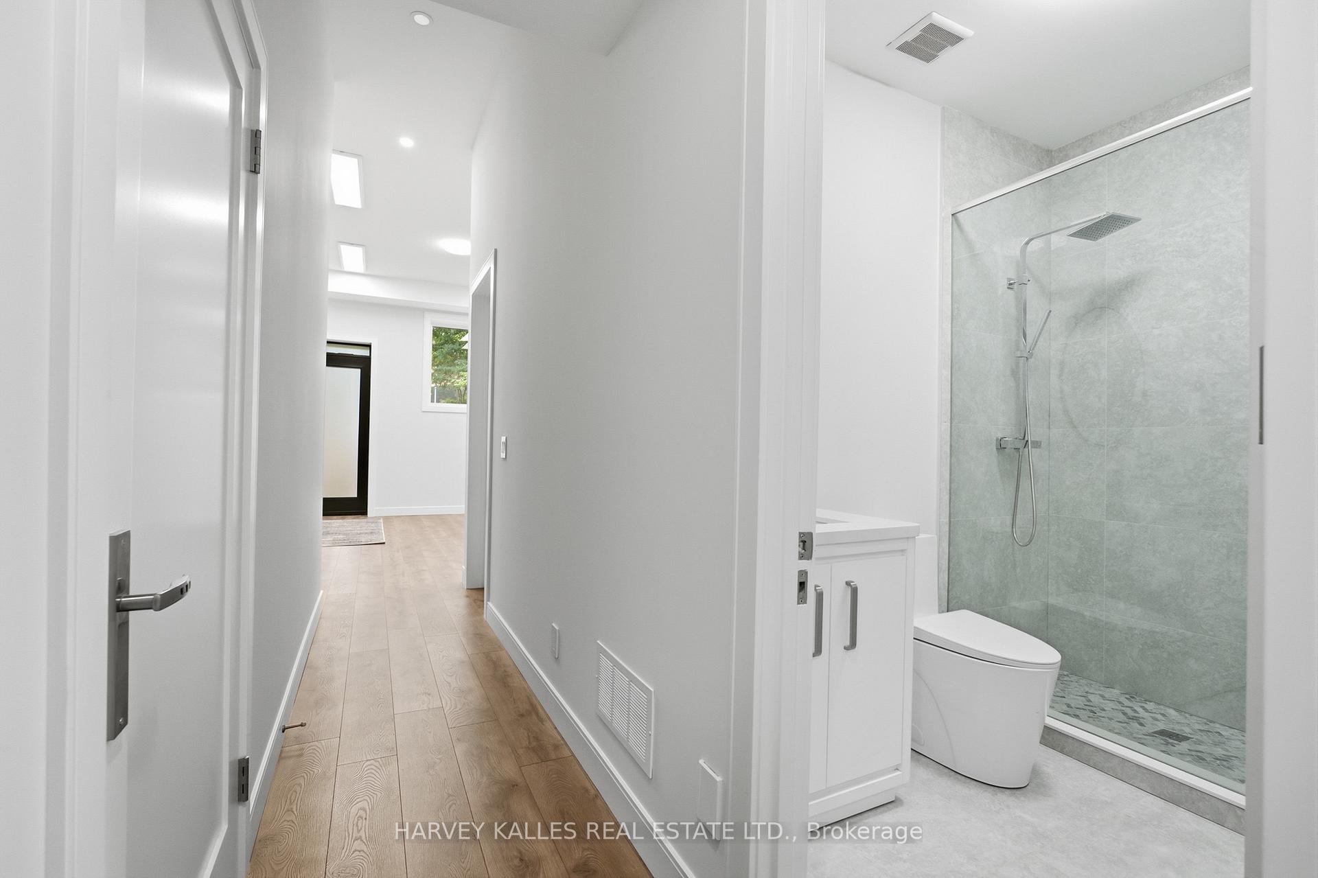 Bright bathroom with a glass walk-in shower beside a long hallway with light wood flooring.