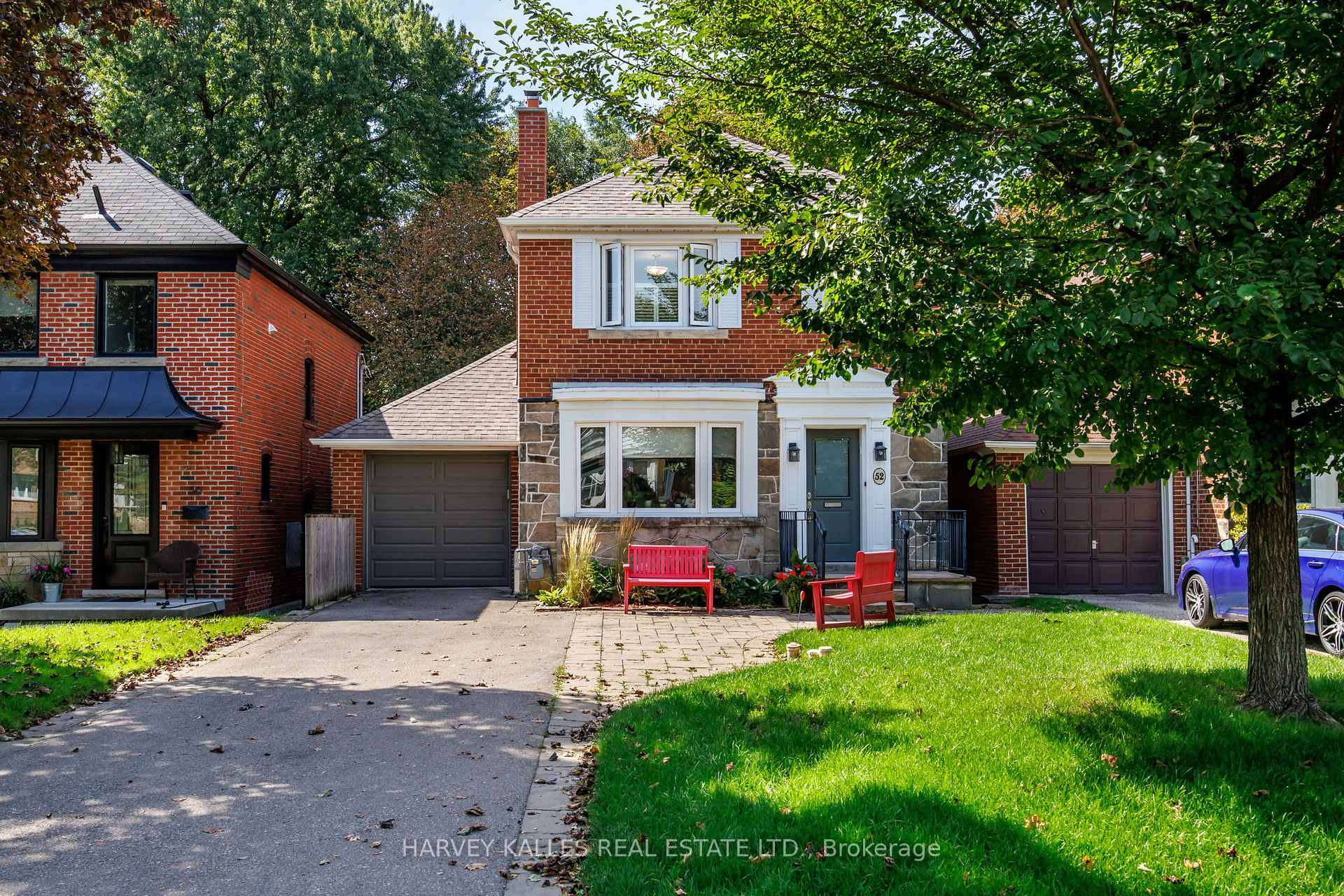 Two-storey brick-and-stone house with an attached garage, red garden chairs, and a leafy front yard.
