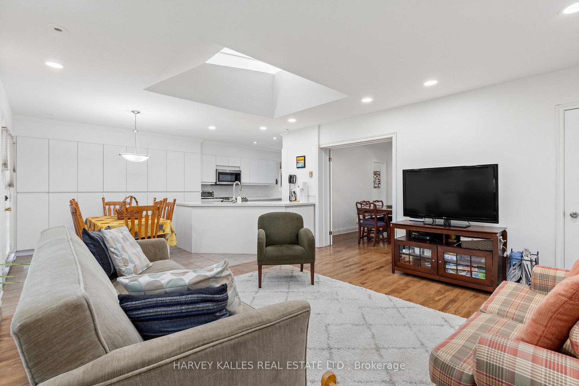 Open-plan living room and kitchen with a large skylight, hardwood floors, and a dining area.
