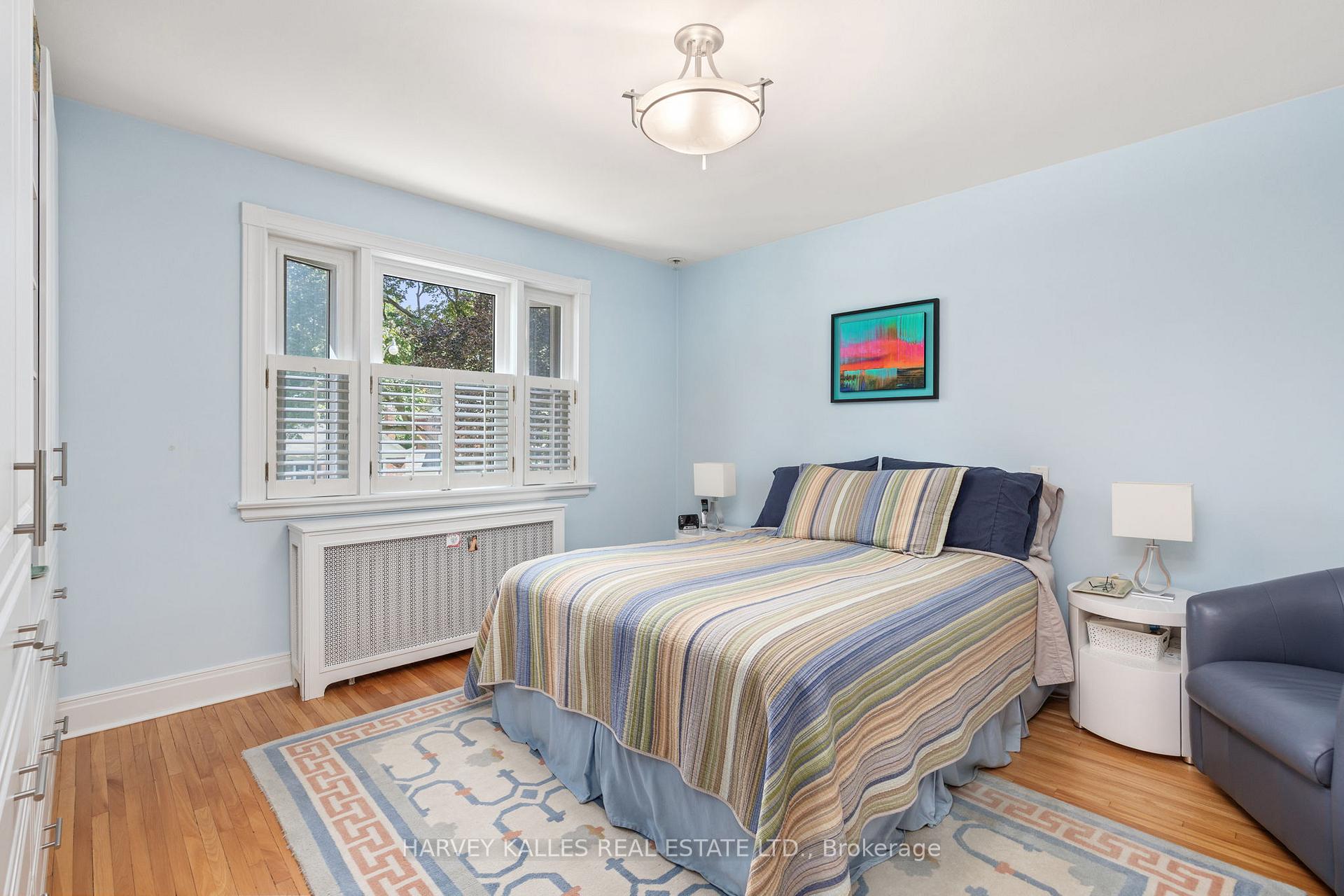 Bedroom with pale blue walls, striped bedding, hardwood floors, and a shuttered window.
