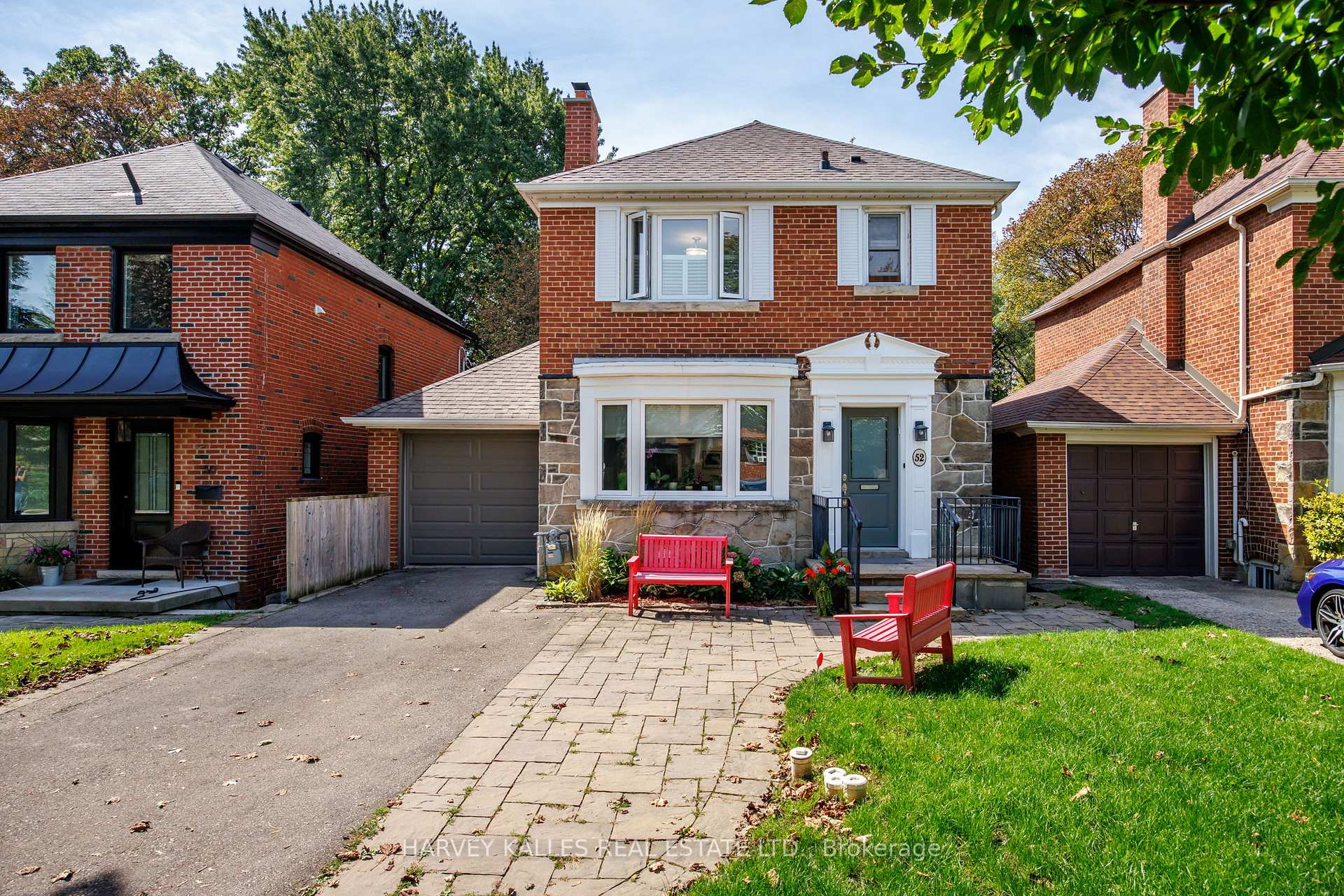 Two-story red-brick house with a stone facade, attached garage, and red benches by the front walkway.
