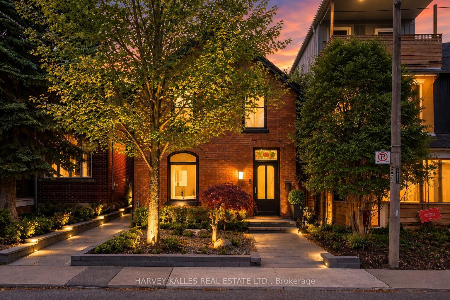 Red-brick home with a black front door, arched window, and landscaped garden at dusk.