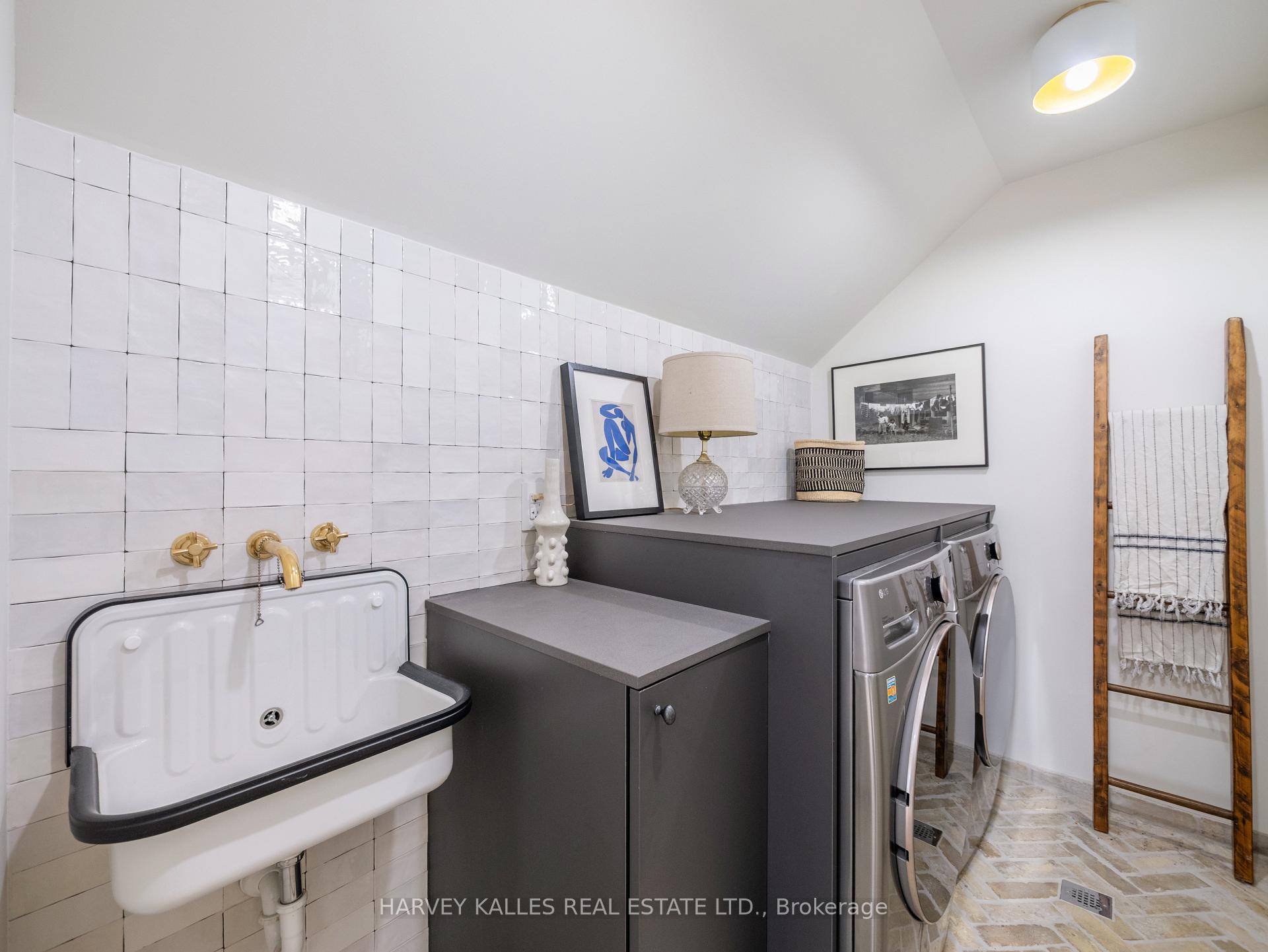 Laundry room with tiled wall, utility sink, dark cabinetry, and front-loading washer and dryer.
