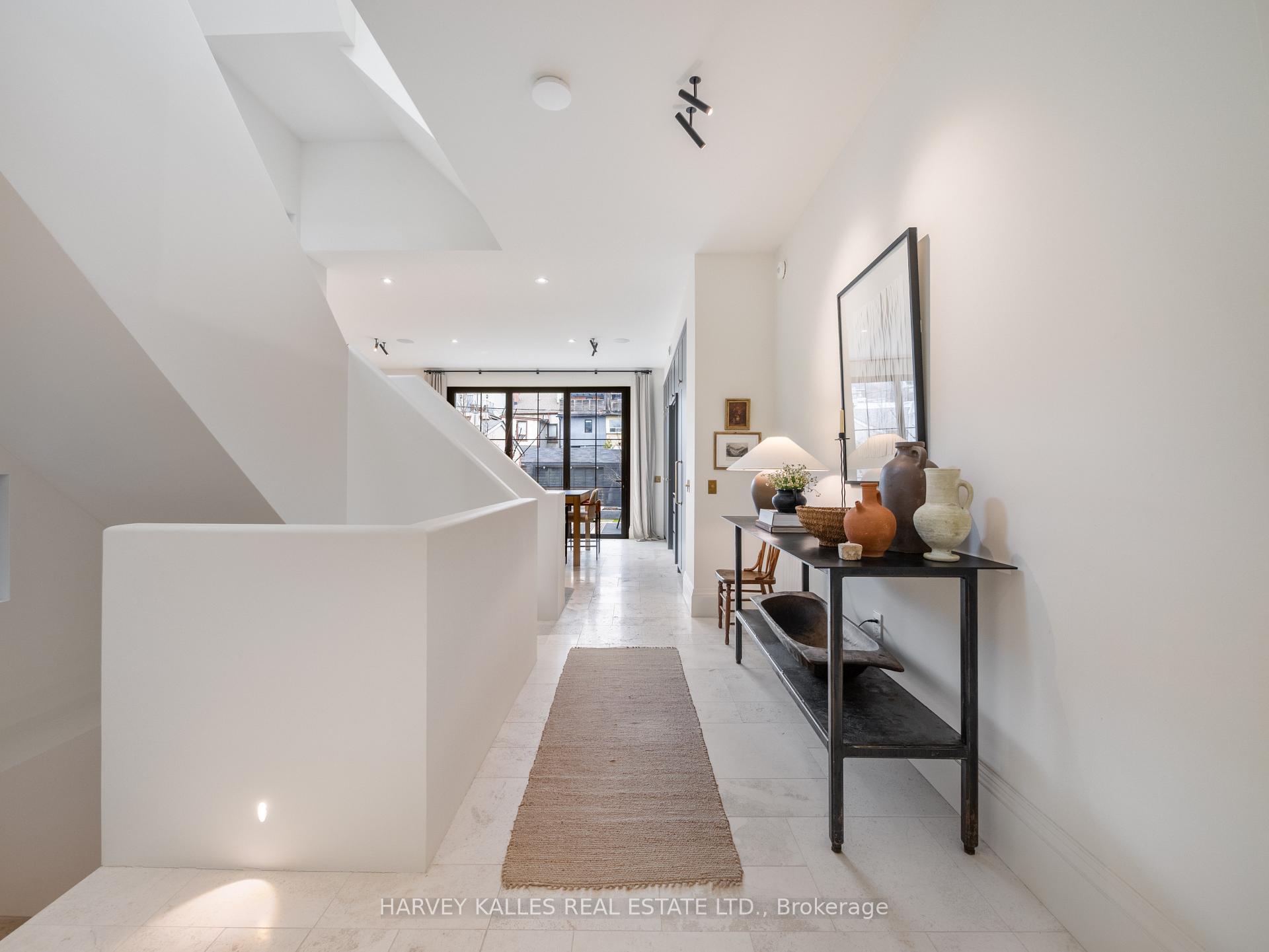 Bright hallway with a stairwell opening, tiled floor, and console table topped with pottery.