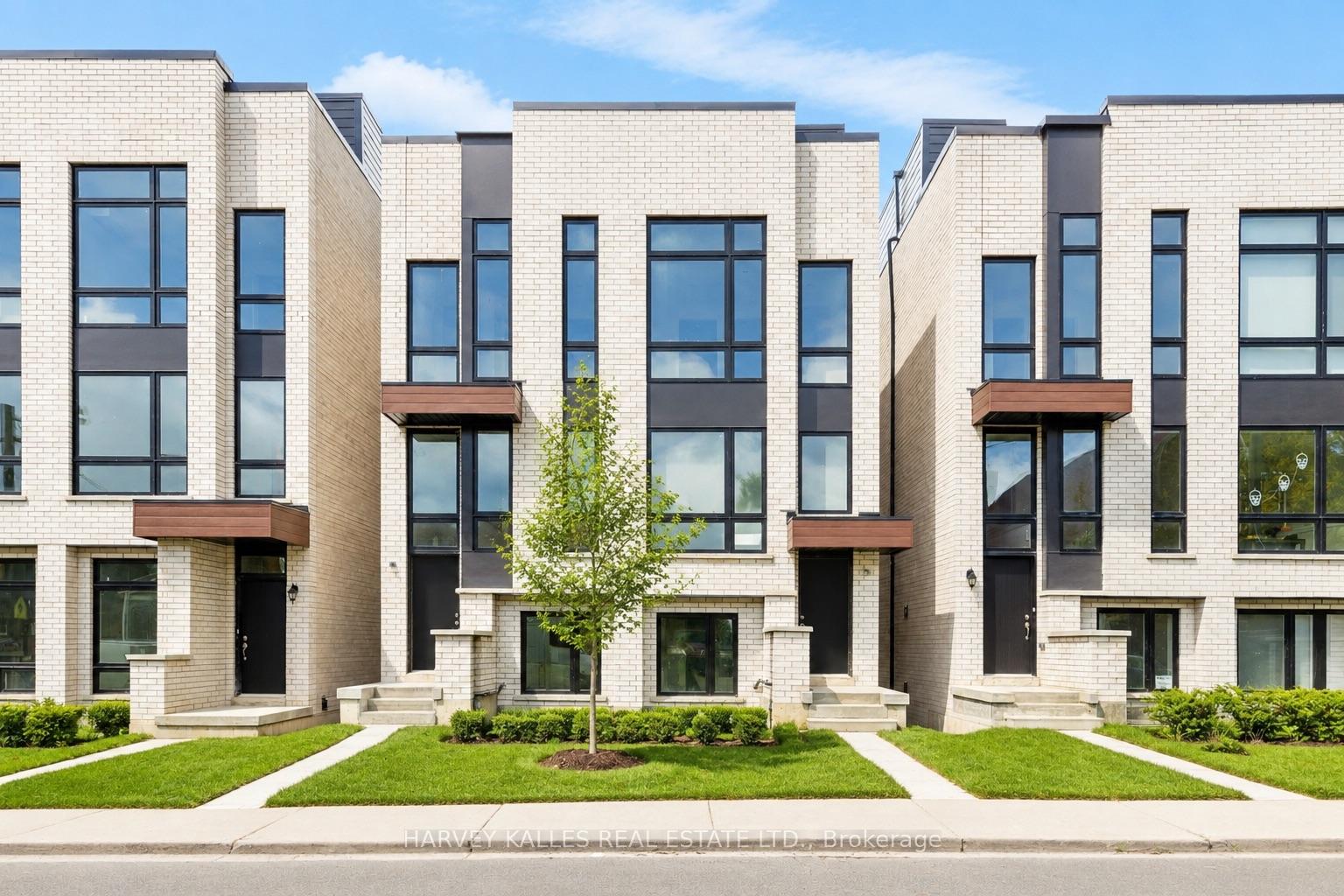 Modern white-brick townhomes with dark-framed windows, wood-toned entry canopies, and landscaped front lawns.
