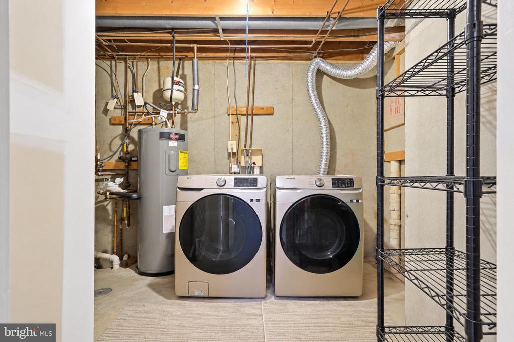 Basement laundry room with front-loading washer and dryer beside a water heater and wire shelving.