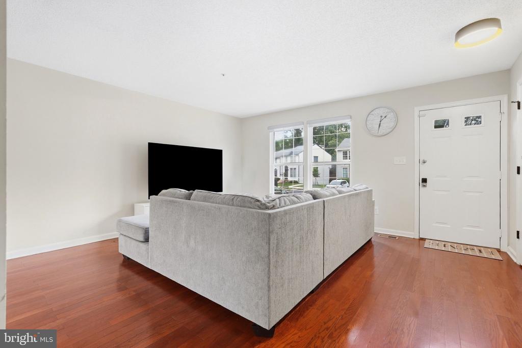 Living room with a gray sectional, wall-mounted television, and reddish hardwood floors.