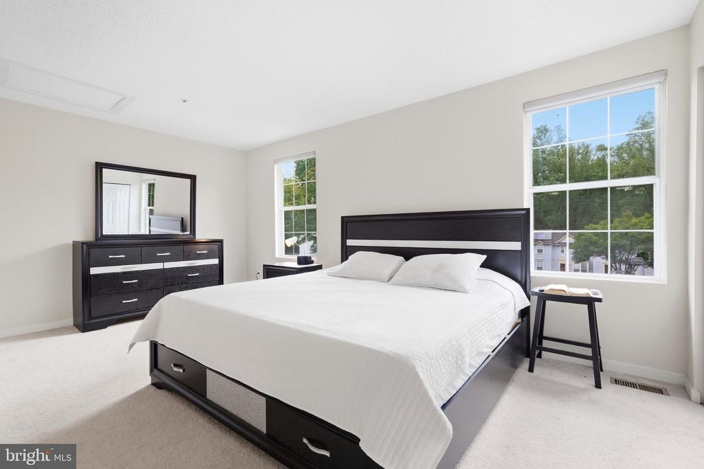 Bright bedroom with a black storage bed, white bedding, and large windows overlooking trees.
