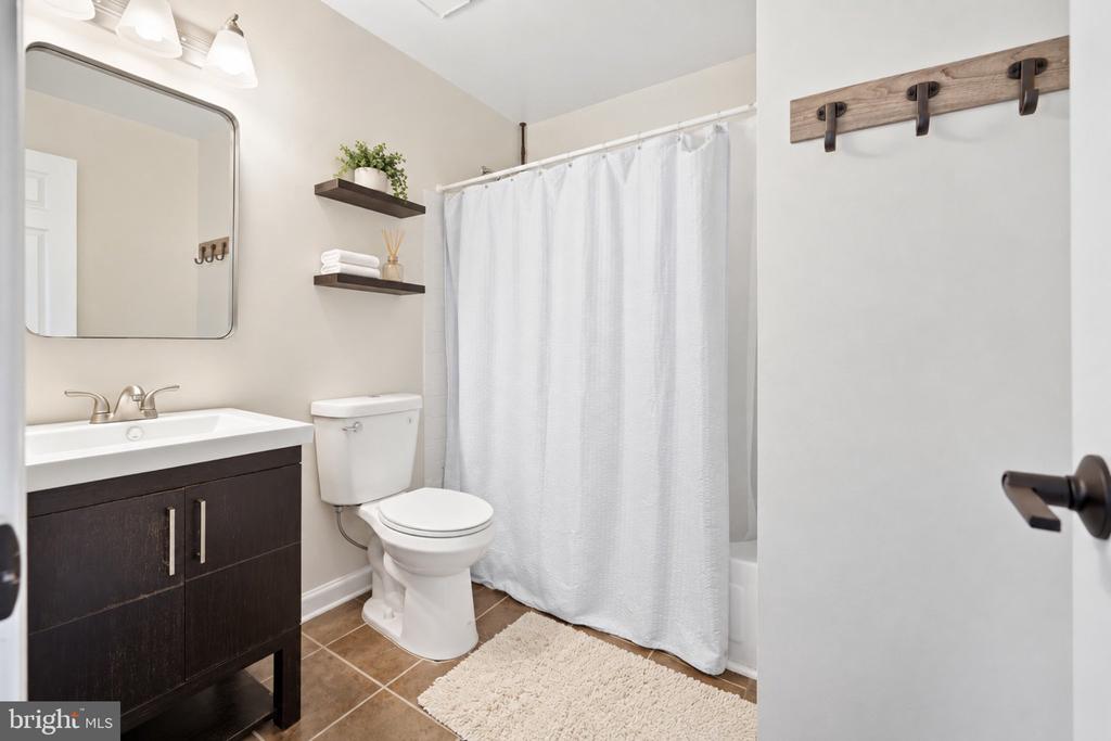 Bathroom with a dark wood vanity, white shower curtain, and brown tile floor.