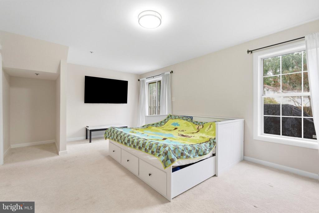 Bedroom with a white drawer bed, colorful bedding, wall-mounted television, and two windows.