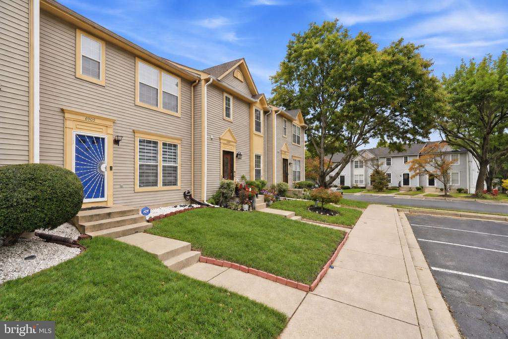 Beige townhouse with a blue decorative front door, landscaped lawn, and sidewalk.