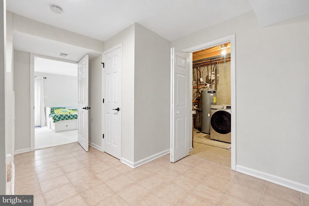 Tiled hallway opening to a bedroom and utility room with a washer and water heater.