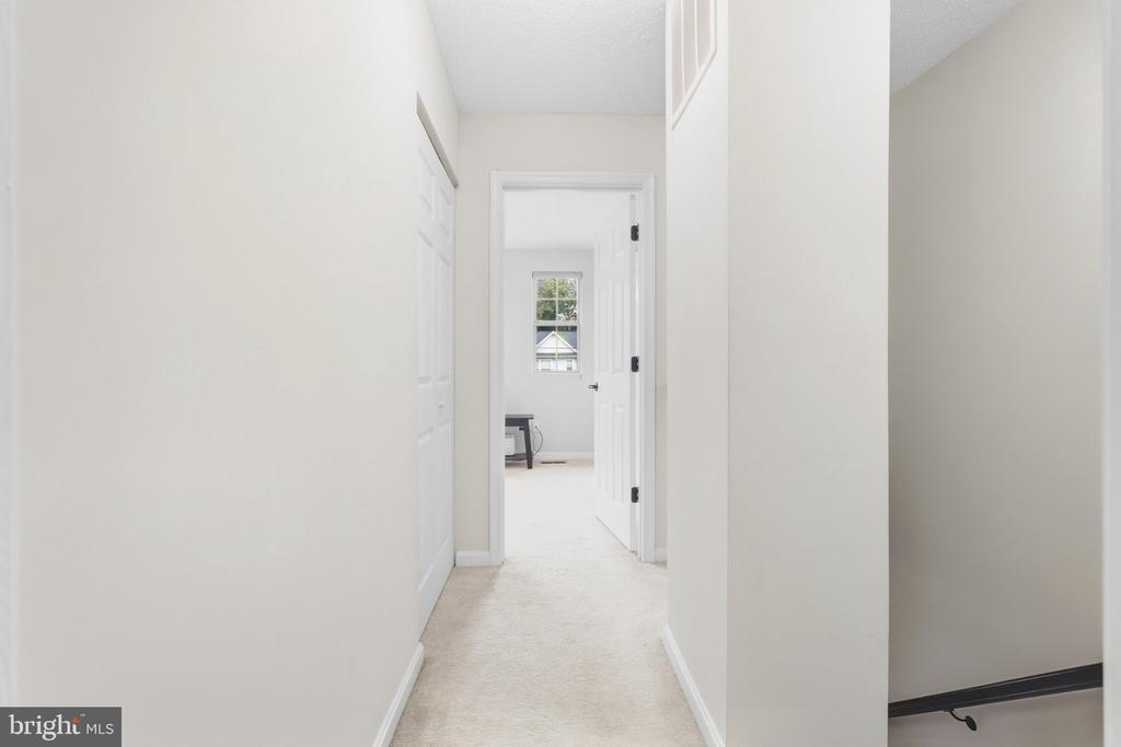 Upstairs hallway with light carpeting, white walls, and a view into a room at the end.