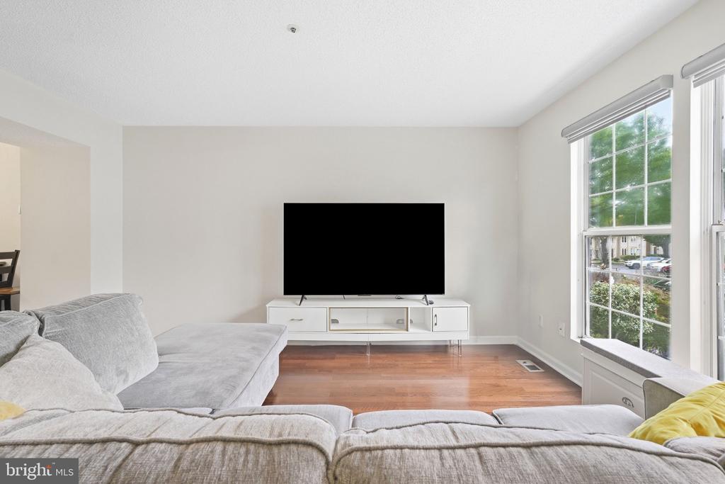 Living room with a gray sectional, white media console, hardwood floors, and large windows.
