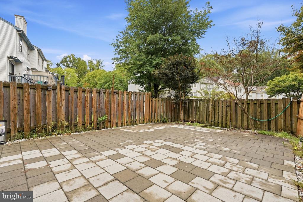 Backyard patio with stone pavers, wooden privacy fence, mature trees, and a garden hose.