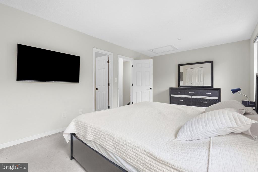 Furnished bedroom with white bedding, a wall-mounted television, and a dark dresser with mirror.