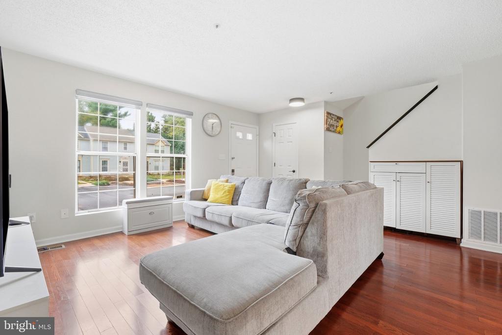 Furnished living room with a gray sectional, hardwood floors, tall windows, and built-in storage beneath the stairs.