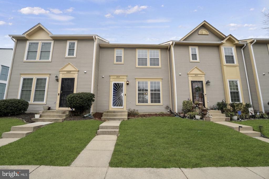 Attached townhouse with gray-beige siding, a black front door, and a walkway across the lawn.