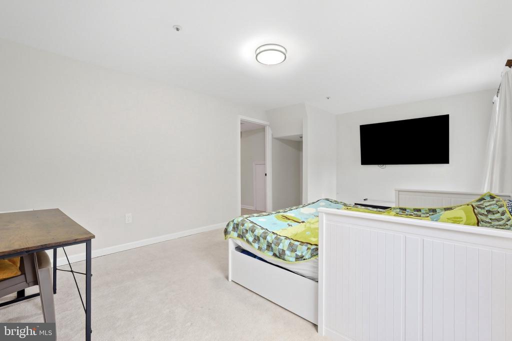 Bedroom with a white paneled bed, colorful bedding, and wall-mounted television.
